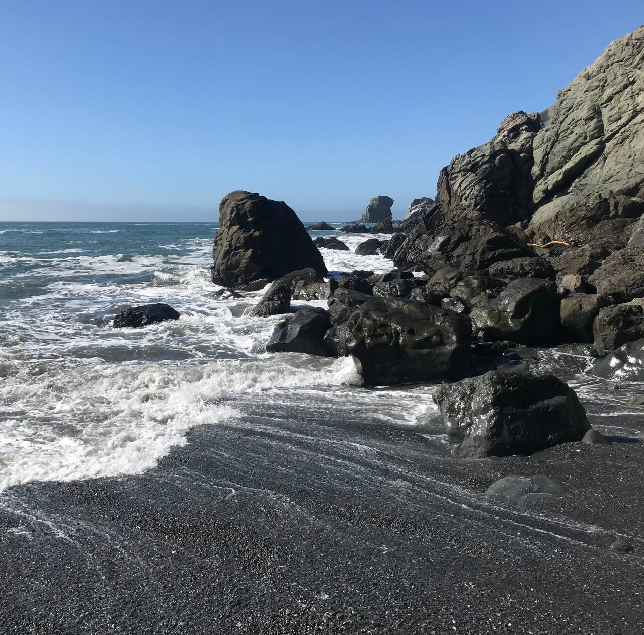 Waves recede after crashing against rocks on a black sand beach