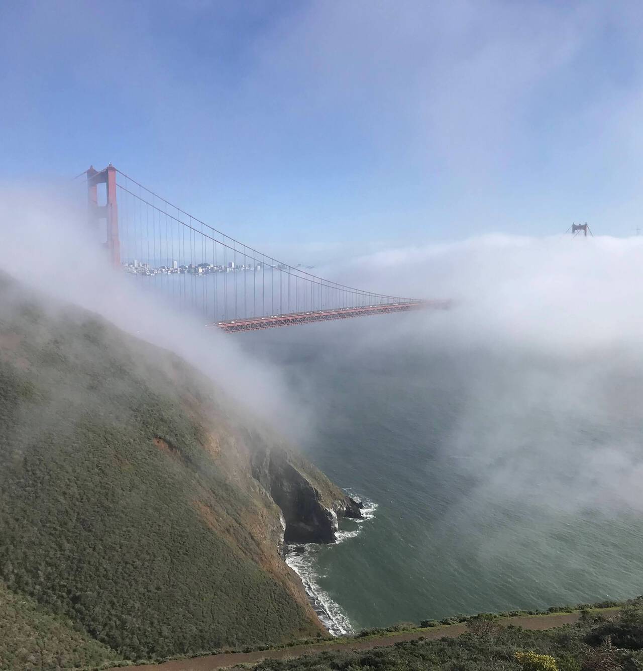 Fog obcures the majority of the Golden Gate Bridge with the ocean visible far below