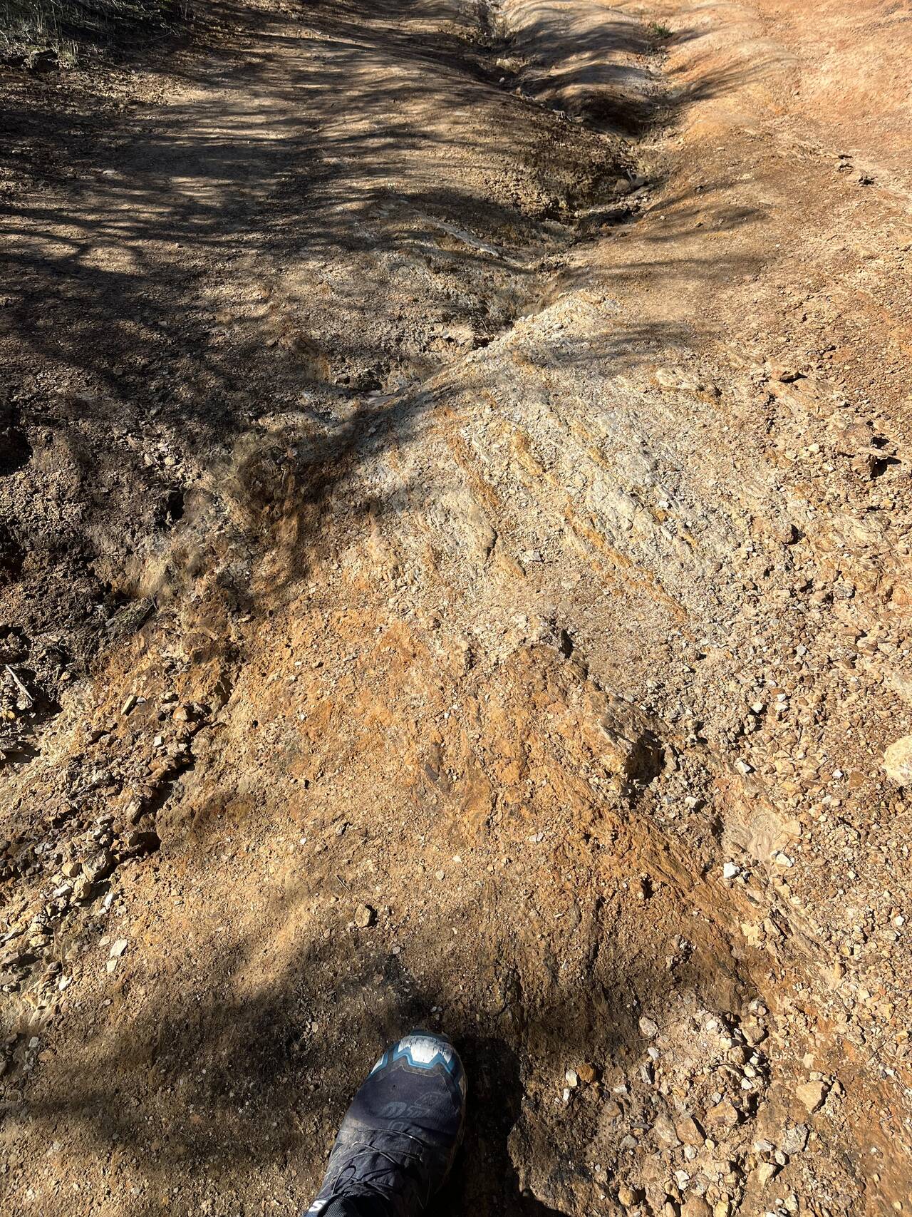 A rocky trail fills the whole picture with a single shoe visible at the bottom.