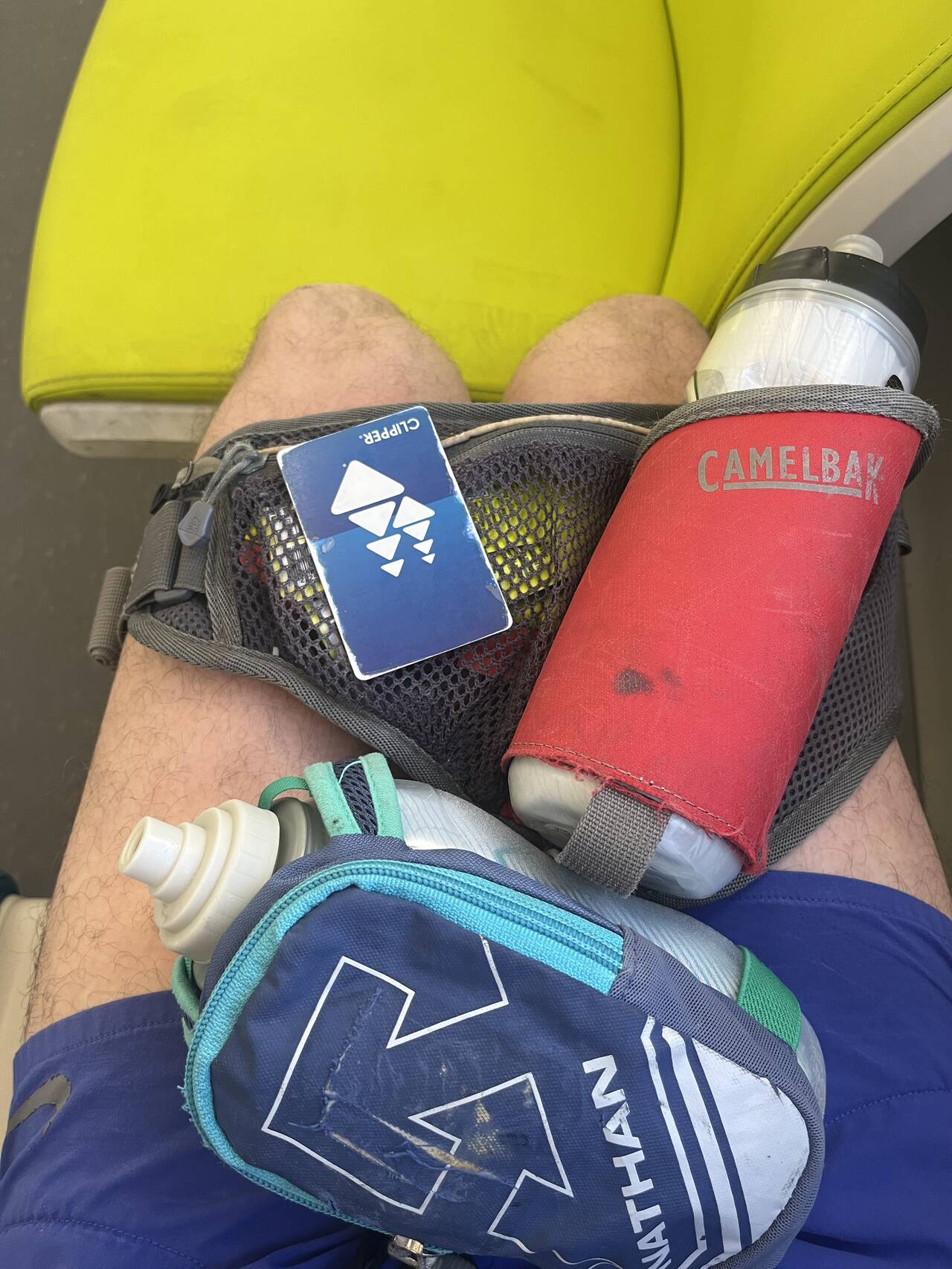 A view of my legs as I sit on the BART. A water bottle, a hand-carry water bottle, and a Clipper card rest on my lap.