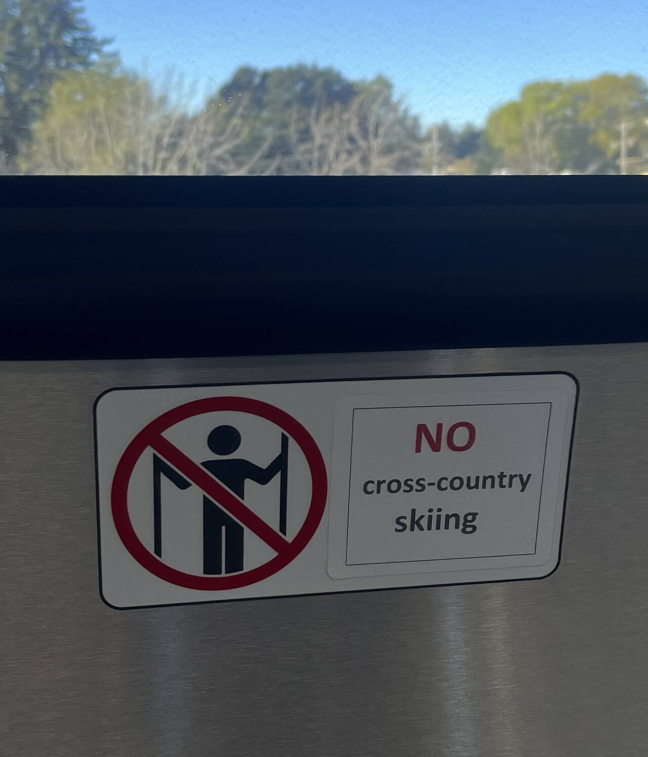 A photo of the BART door. A diagram shows a person holding the doors open, but it looks more like someone holding cross-country skiis. A sticker is pasted over the original text which reads "NO cross-country skiing."