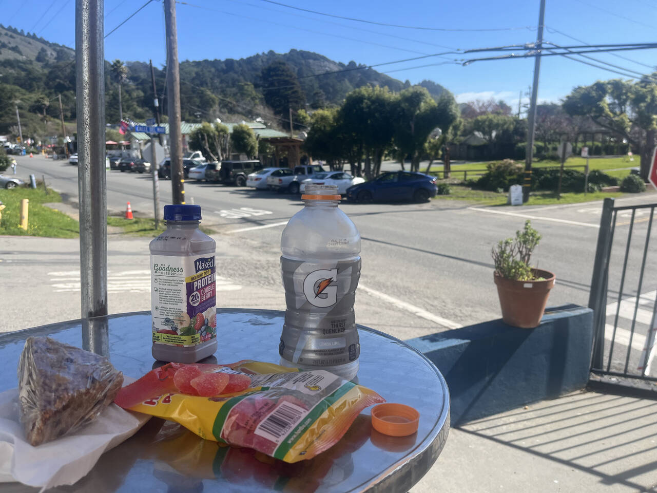 Haribo gummy bears, an oat bar, a Gatorade, a smoothie, and a ginger molasses cookie sit on a table. The main intersection in Stinson Beach is visible in the background.